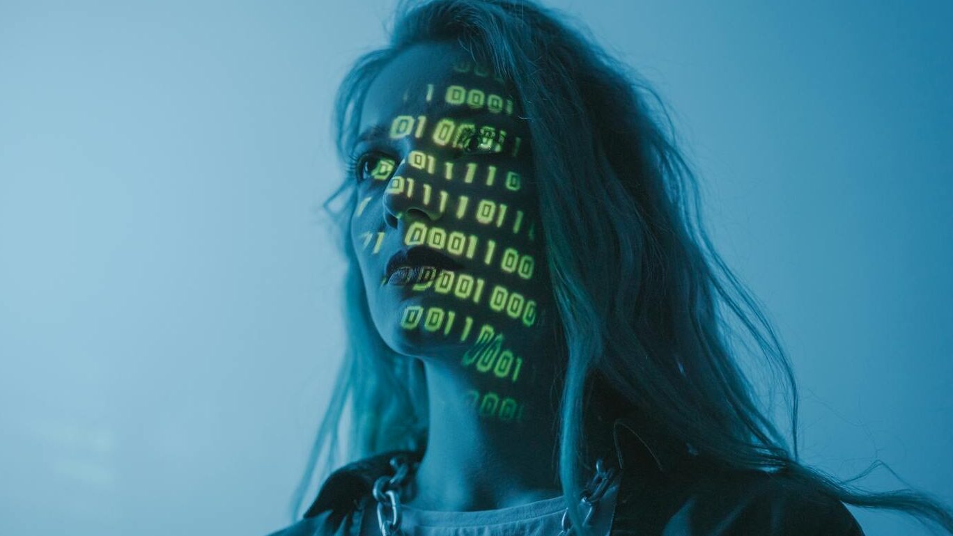 A woman with binary code lights projected on her face, symbolizing technology.